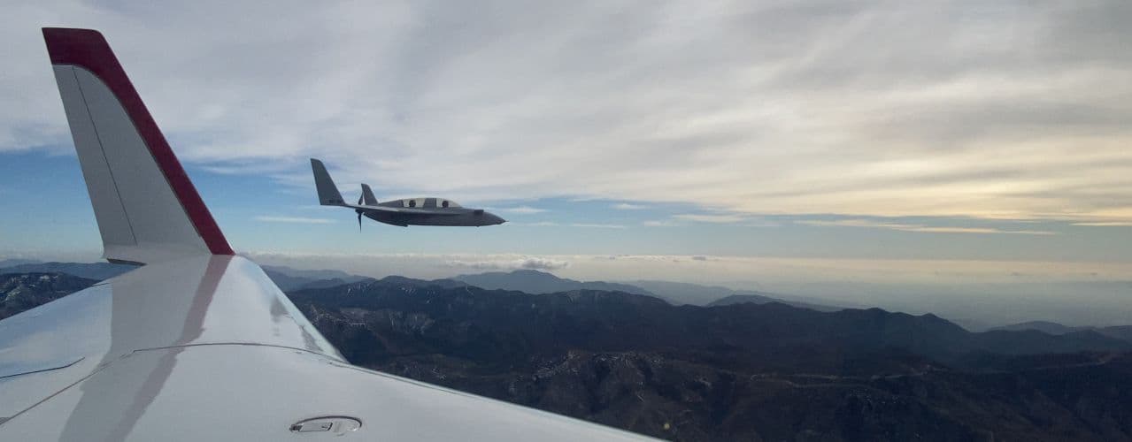 A trainer aircraft flying over mountains, seen from another aircraft's wing